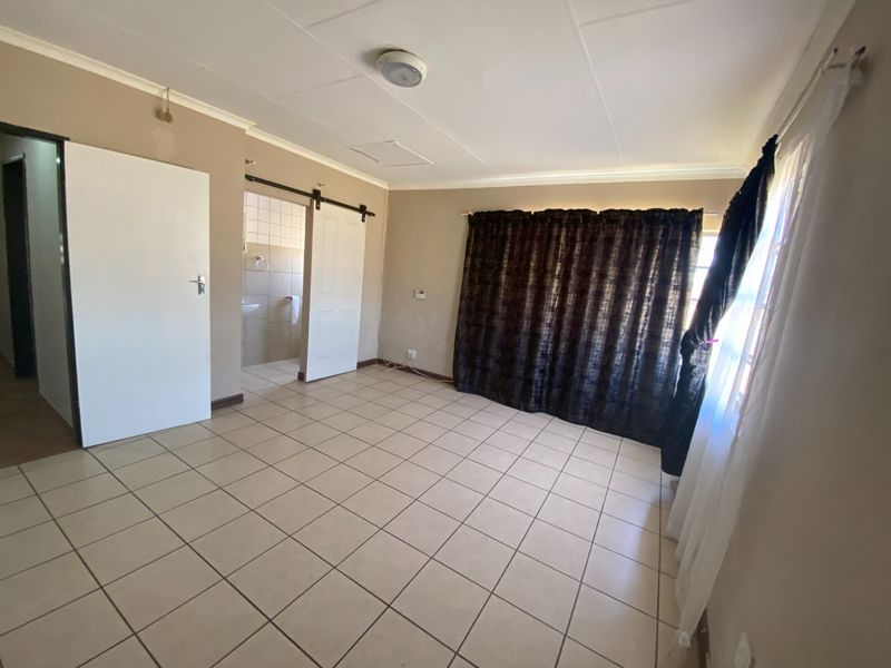 An empty bedroom featuring tiled flooring, a sliding barn door leading to an en-suite bathroom, and neutral wall finishes.