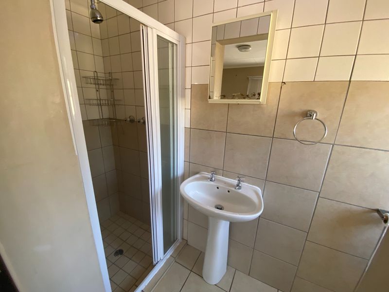 A functional bathroom featuring a shower enclosure, pedestal basin, and neutral wall and floor tiling.