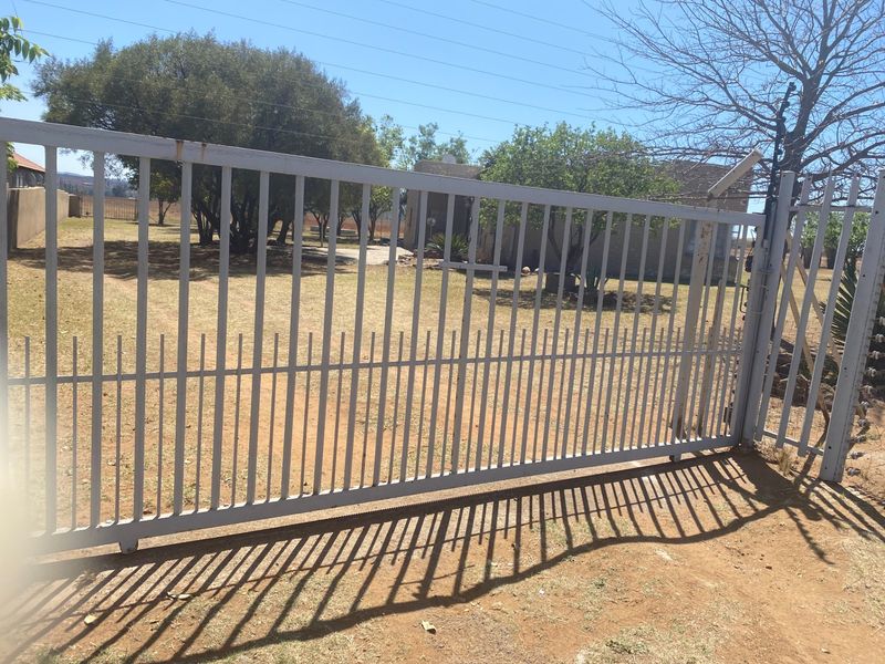 View of the property entrance featuring a sliding security gate and perimeter electric fencing on a small holding.
