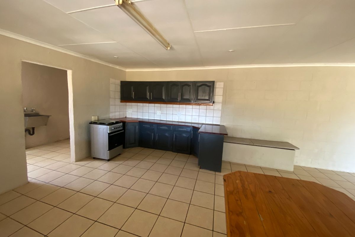 A functional kitchen area featuring dark cabinetry, tiled flooring, and a tiled backsplash, with an adjacent utility space visible through the doorway.