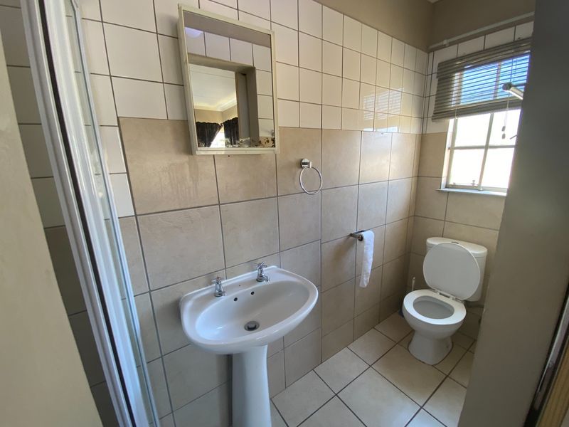 A functional bathroom featuring a pedestal basin, toilet, and shower enclosure with neutral wall and floor tiling.