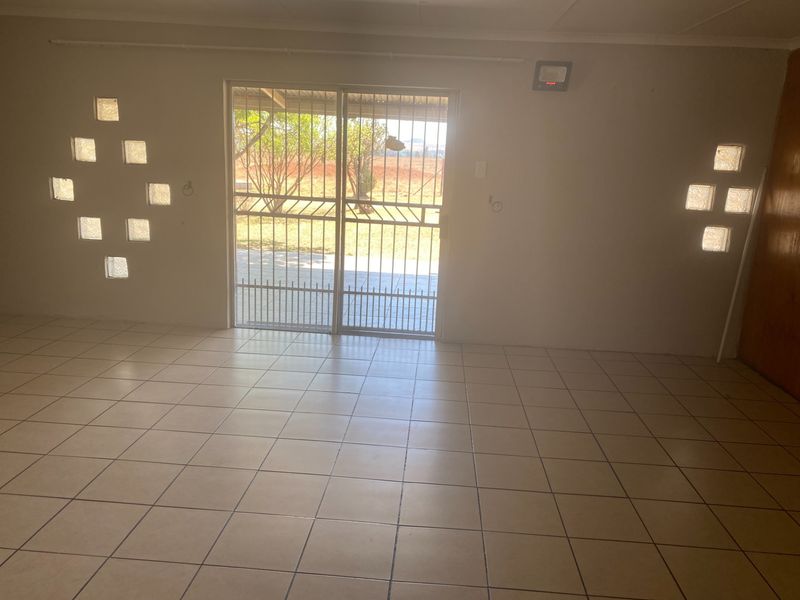 An empty living area featuring tiled flooring, decorative glass block windows, and a sliding door leading to the exterior.