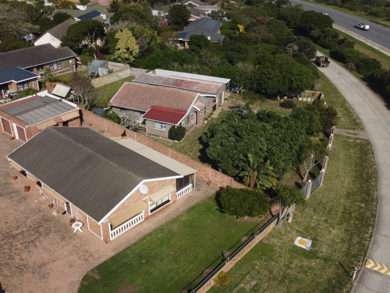 Aerial view of the property showing the main house, paved driveway, surrounding garden, and boundary walls in a suburban setting.
