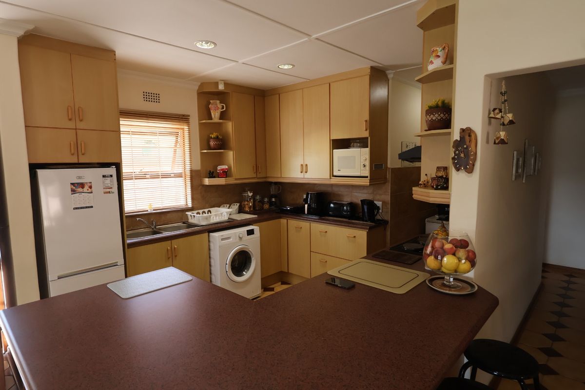 A functional kitchen featuring light wood-tone cabinetry, dark laminate countertops, integrated appliances, and recessed lighting, offering a practical layout for daily meal preparation.