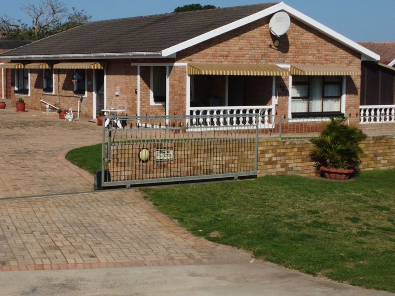 Front view of a single-story brick house featuring a paved driveway, sliding security gate, and a covered patio area with balustrades.