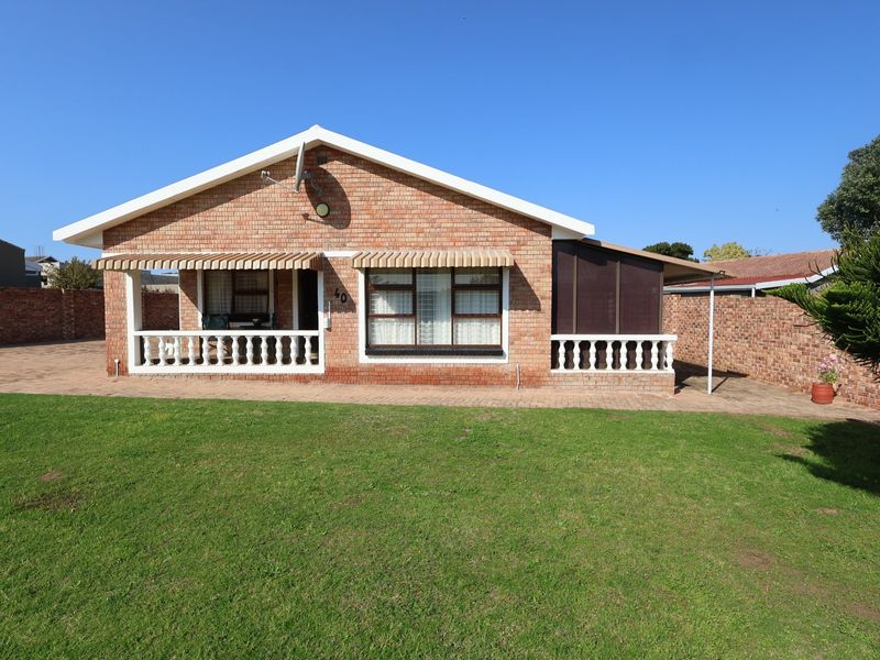 A single-story brick house featuring a covered front patio with balustrades, a paved driveway, and a well-maintained front lawn.