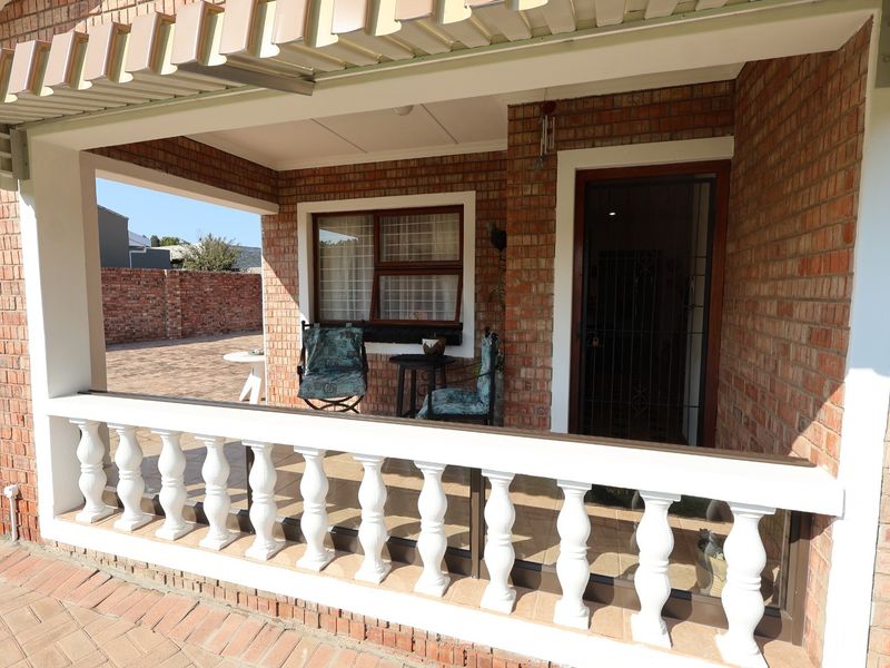 A covered brick patio featuring a classic balustrade, overhead awning, and secure entrance, providing a functional outdoor space for relaxation.
