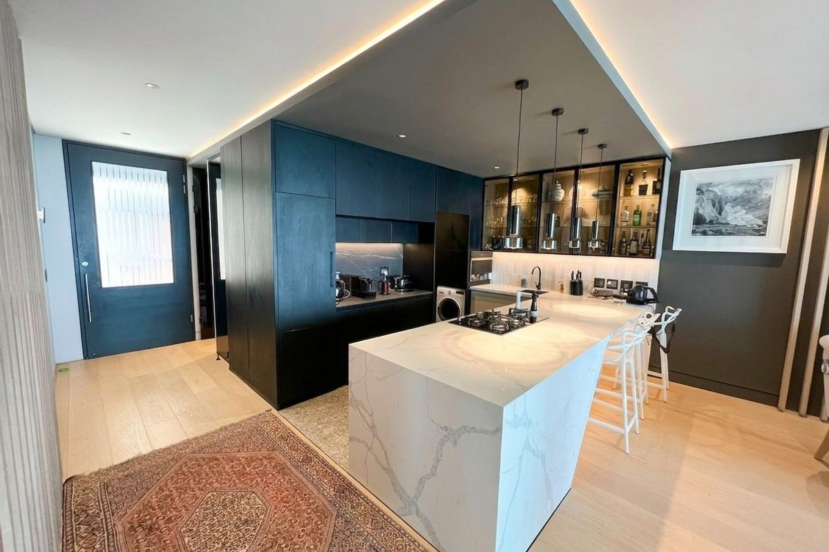 Modern kitchen featuring a large stone-topped island with integrated gas hob, dark custom cabinetry, and elegant recessed ceiling lighting.