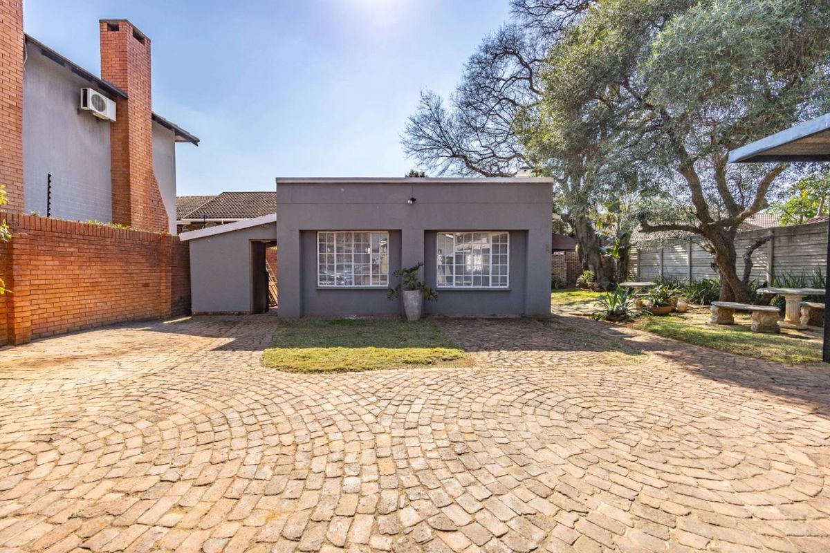 Rear exterior view featuring a spacious brick-paved courtyard, established trees, and a solid brick boundary wall.