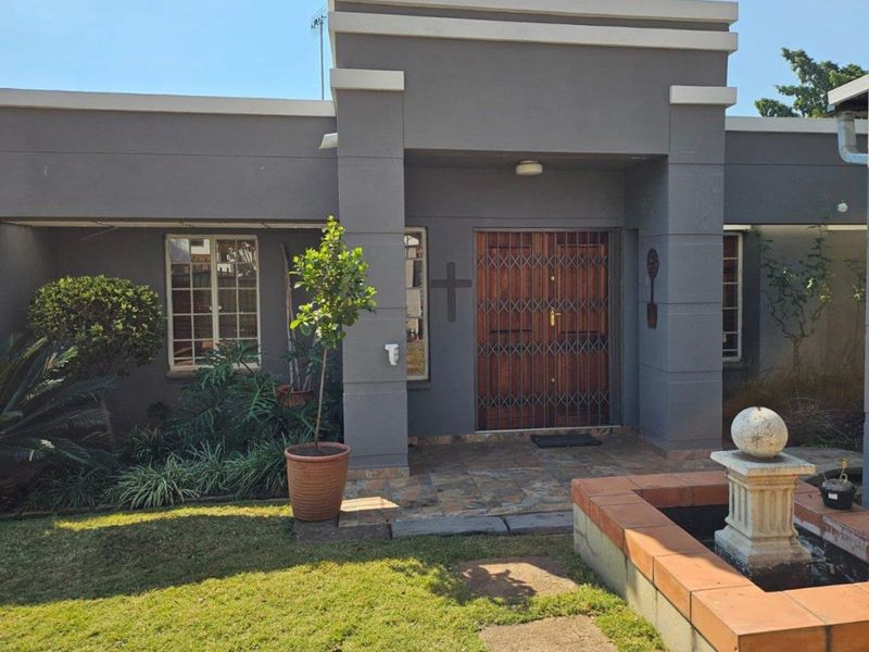 Front facade of the house featuring a covered entrance with a security gate, stone tiled porch, and a landscaped garden with a water feature.