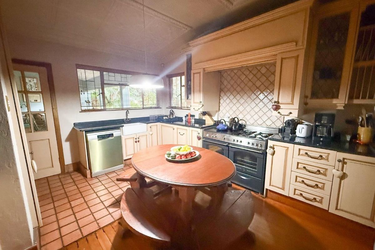 A traditional kitchen featuring farmhouse-style cabinetry, a gas range with an extractor hood, a farmhouse sink, and a mix of timber and tiled flooring.