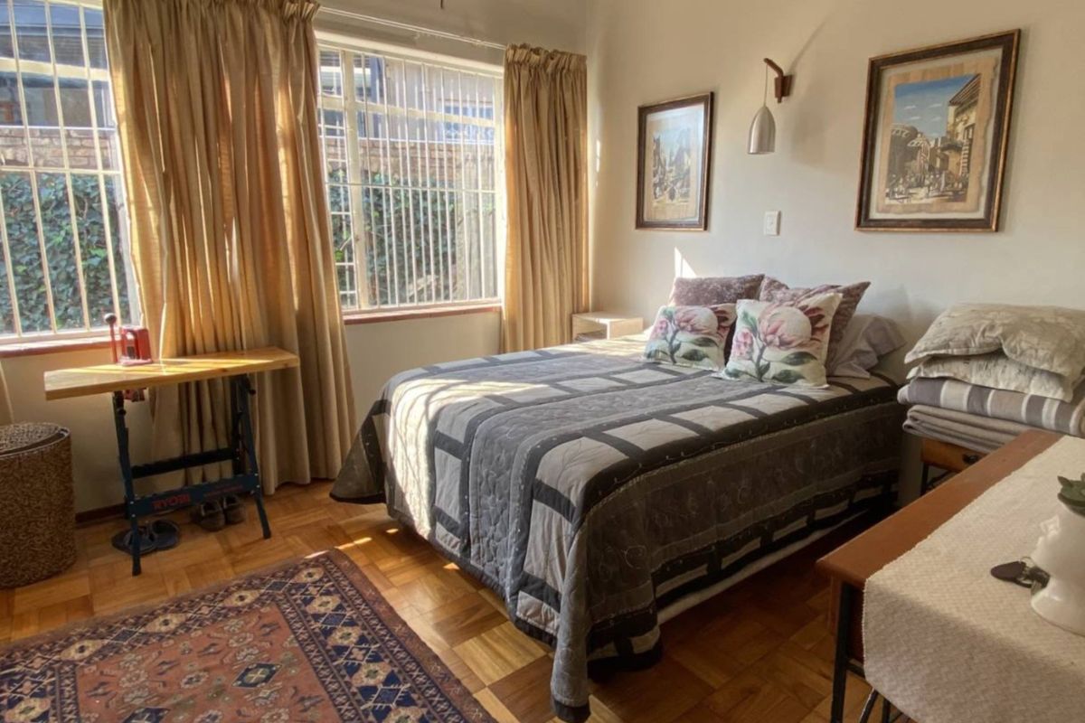 A bedroom featuring parquet flooring and large windows with security bars, providing natural light and a view of the exterior.