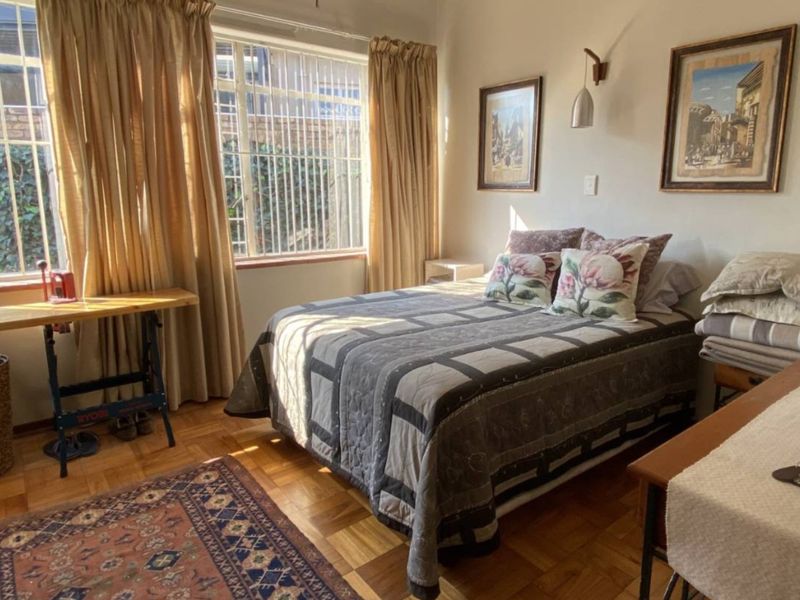 A bedroom featuring parquet flooring and large windows with security bars, providing natural light and a view of the exterior.