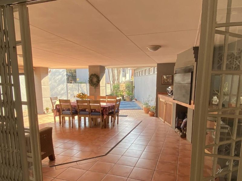 A spacious covered patio featuring tiled flooring and a built-in braai, ideal for outdoor dining and entertaining.