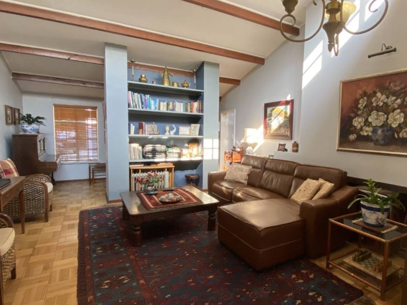 Spacious living room featuring exposed timber ceiling beams, parquet flooring, a built-in shelving unit, and a fireplace, offering a warm and traditional atmosphere.