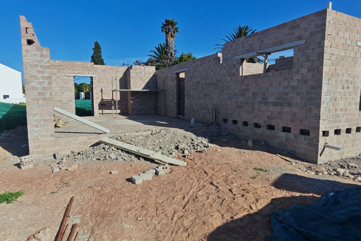 A construction site view showing the brickwork shell of a house under development, featuring exposed masonry walls and concrete lintels.