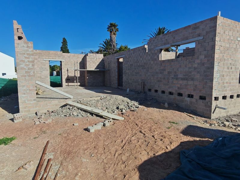 A construction site view showing the brickwork shell of a house under development, featuring exposed masonry walls and concrete lintels.