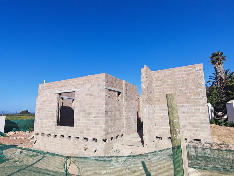 A construction site showing the early stages of a masonry house structure with exposed concrete block walls and foundation vents.