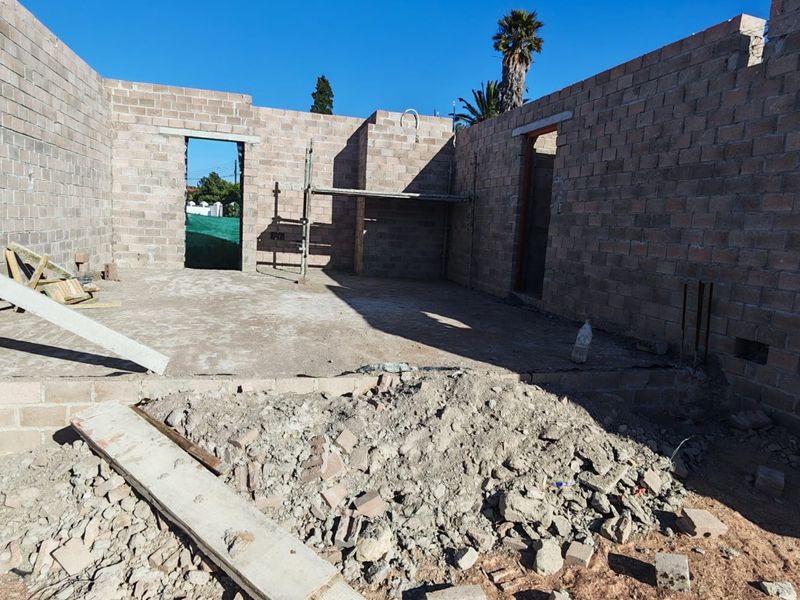 An unfinished construction site showing exposed concrete block walls and a concrete slab foundation, currently in the early stages of building development.