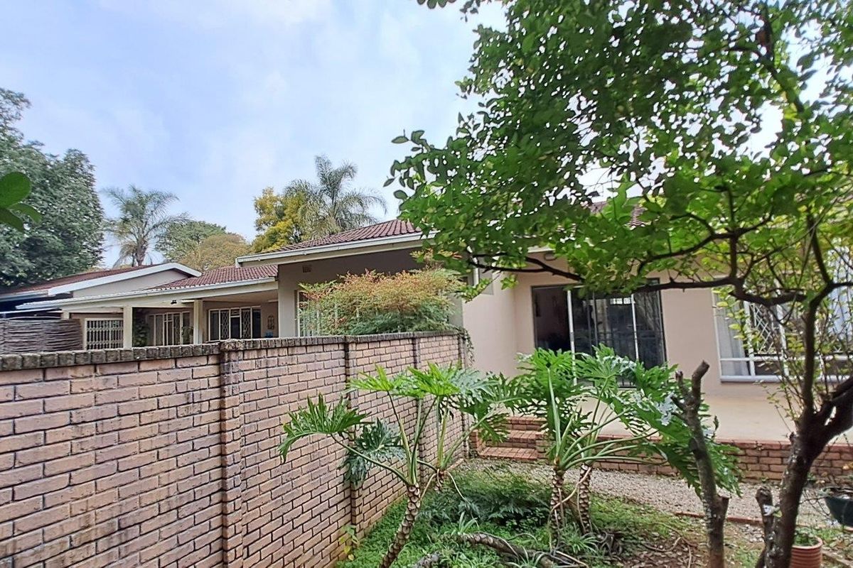 Rear view of the property featuring a paved patio, sliding glass doors, and a brick boundary wall within a garden setting.