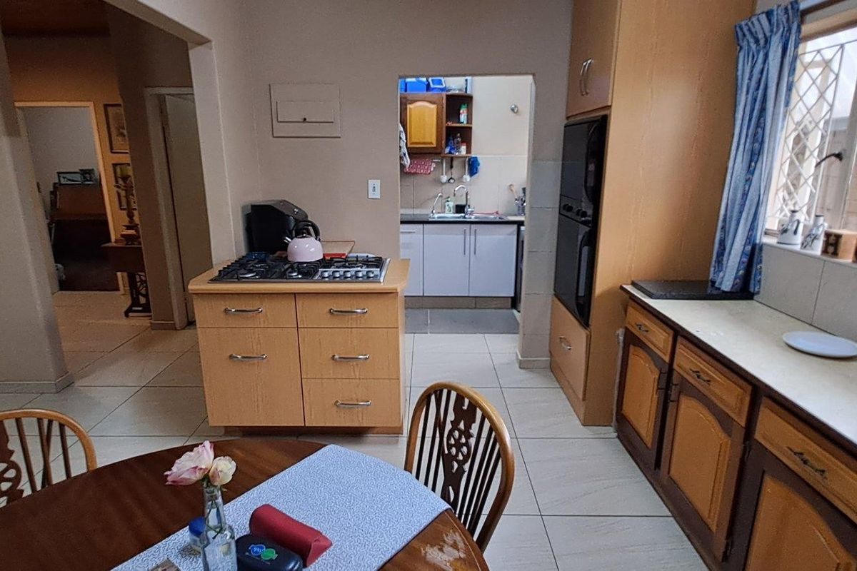 A functional kitchen featuring built-in cabinetry, a central island with a gas hob, and an integrated oven, with an adjoining scullery area.