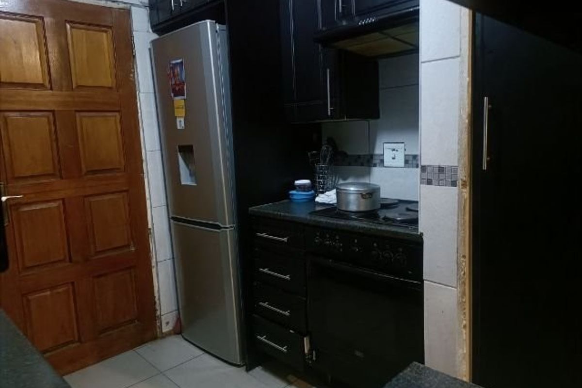 A compact kitchen area featuring dark cabinetry, a built-in oven and hob, and tiled finishes, requiring some maintenance and cosmetic updates.