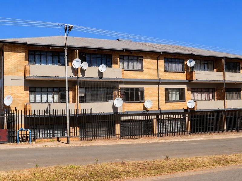 A multi-story apartment building featuring a face brick facade, private balconies, and secure perimeter fencing along the street front.