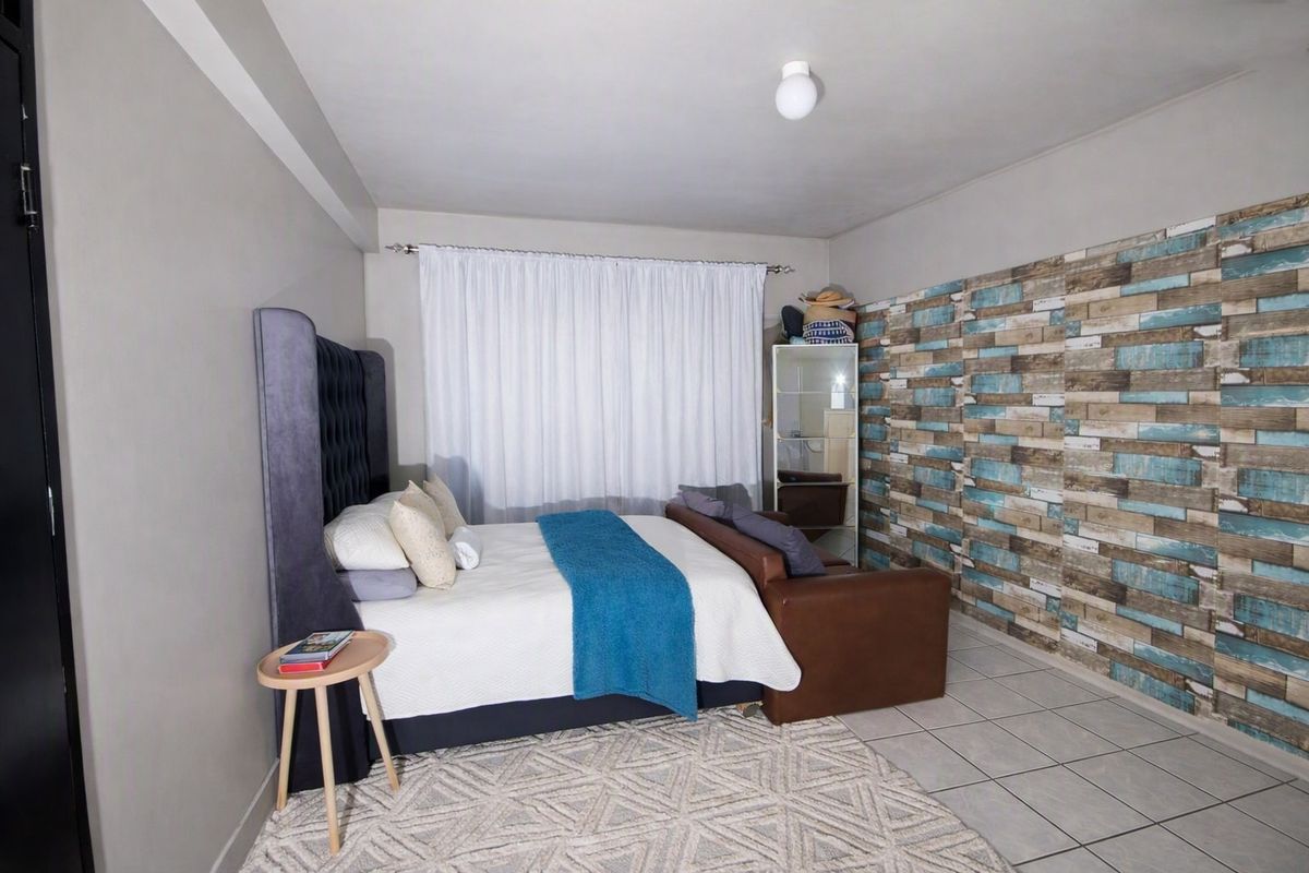 A bedroom featuring tiled flooring, a curtain rod, and a ceiling light fixture, with a decorative accent wall.