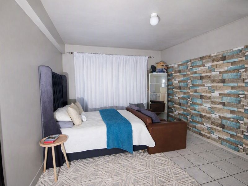 A bedroom featuring tiled flooring, a curtain rod, and a ceiling light fixture, with a decorative accent wall.