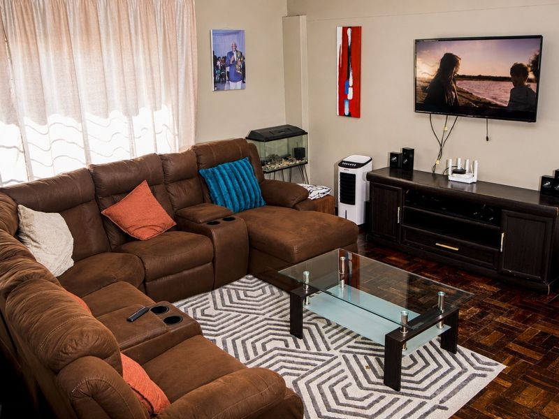 A comfortable living room featuring classic parquet flooring and large windows with curtain tracks, providing a warm and functional space.