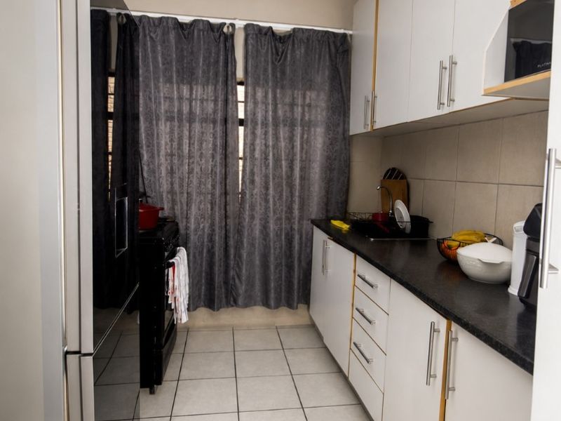 A functional galley-style kitchen featuring white cabinetry, dark countertops, tiled flooring, and a tiled backsplash.
