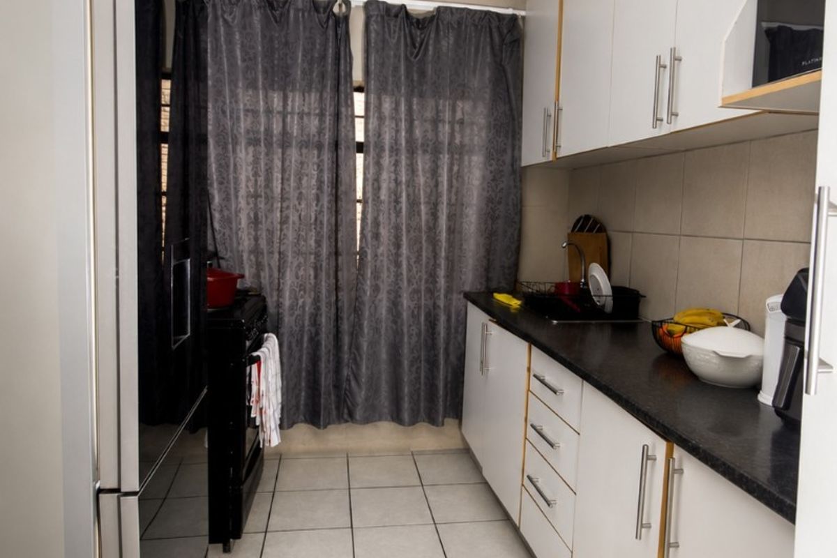 A functional galley-style kitchen featuring white cabinetry, dark countertops, tiled flooring, and a tiled backsplash.