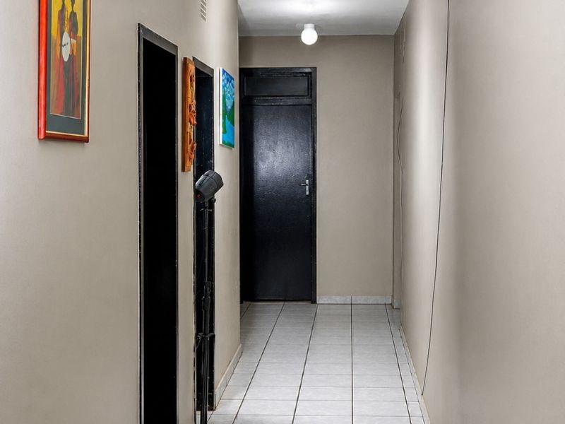 A functional apartment hallway featuring neutral wall tones, tiled flooring, and multiple internal access doors.