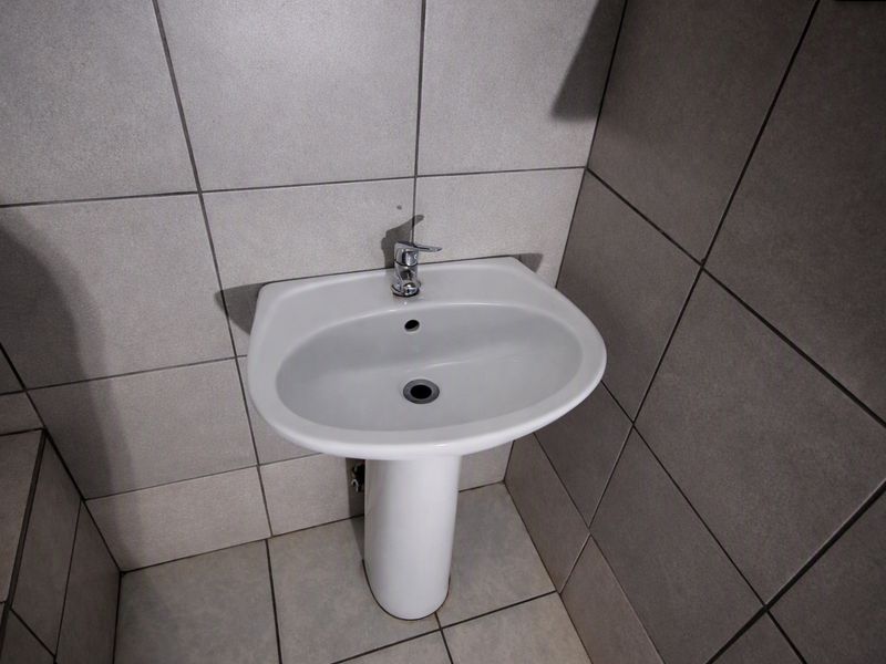 A clean, modern bathroom featuring a white pedestal basin with a chrome mixer tap, complemented by neutral grey ceramic wall and floor tiles.