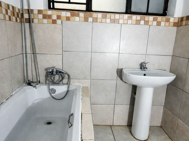 A functional bathroom featuring a bathtub, pedestal basin, and neutral wall and floor tiling, requiring some maintenance and cosmetic updates.
