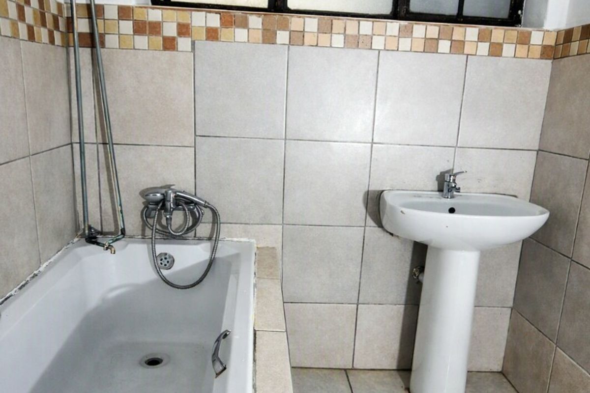 A functional bathroom featuring a bathtub, pedestal basin, and neutral wall and floor tiling, requiring some maintenance and cosmetic updates.