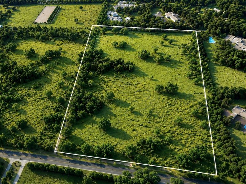 An aerial view of a large, rectangular vacant residential plot featuring established trees and clear boundary lines, situated in a developed neighborhood.