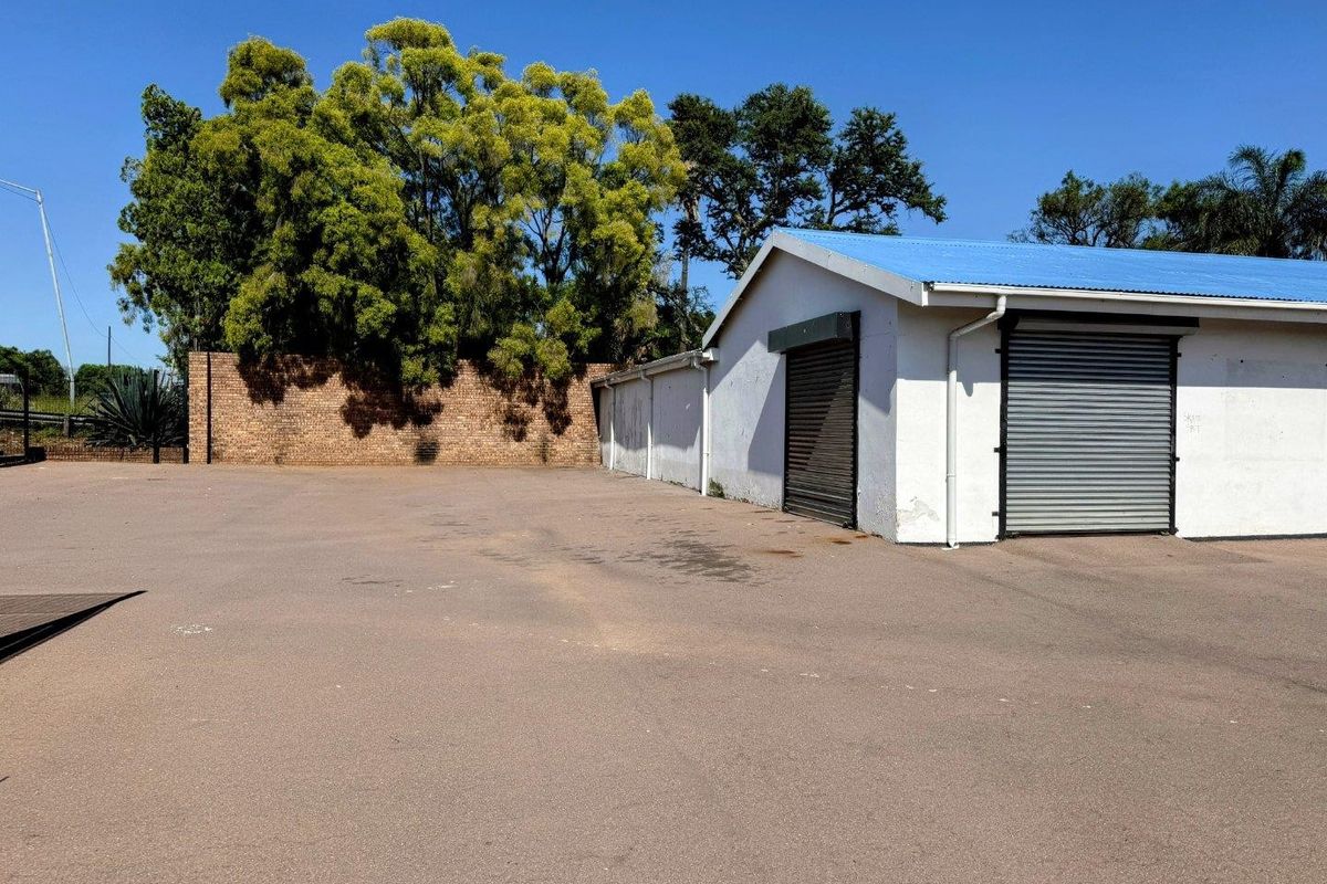 Commercial exterior yard space featuring asphalt paving, a brick boundary wall, and a building structure with metal roller shutter doors.
