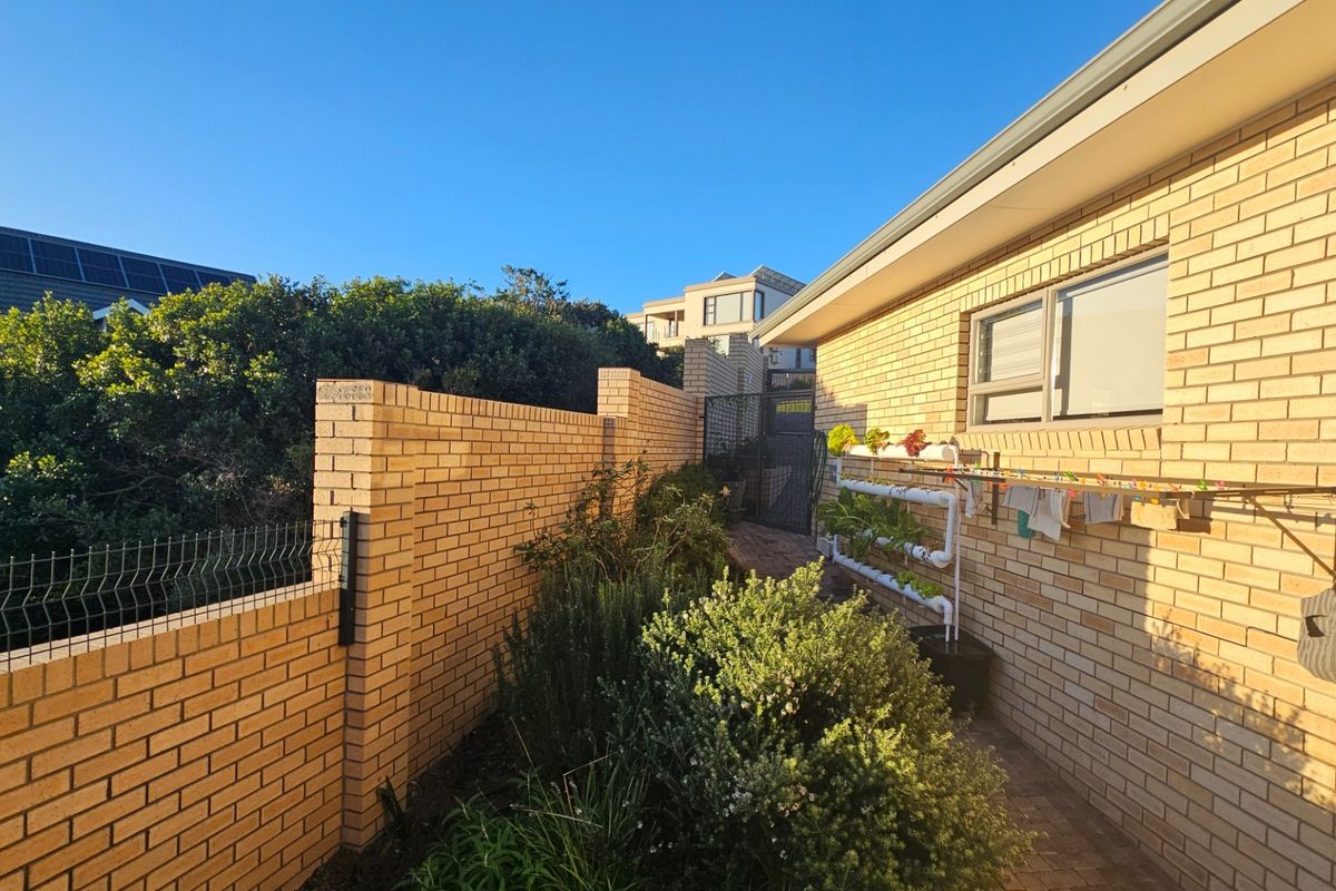 A well-maintained rear exterior area featuring a brick boundary wall, paved pathway, and secure gated access along the side of the house.