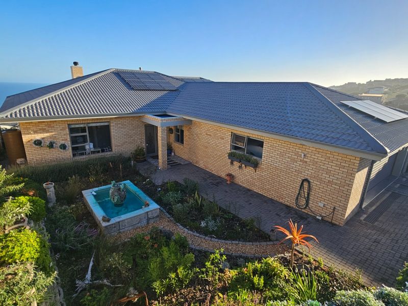 A well-maintained brick house featuring a tiled roof with solar panels, a paved driveway, and a landscaped front garden with a water feature.