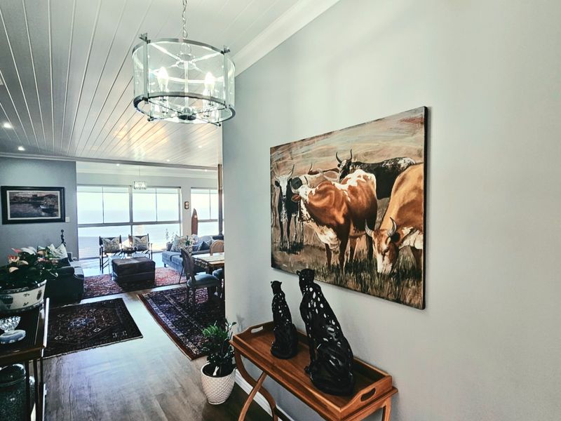 A bright, welcoming hallway featuring a tongue and groove ceiling and modern pendant lighting, leading into an open-plan living area with ocean views.