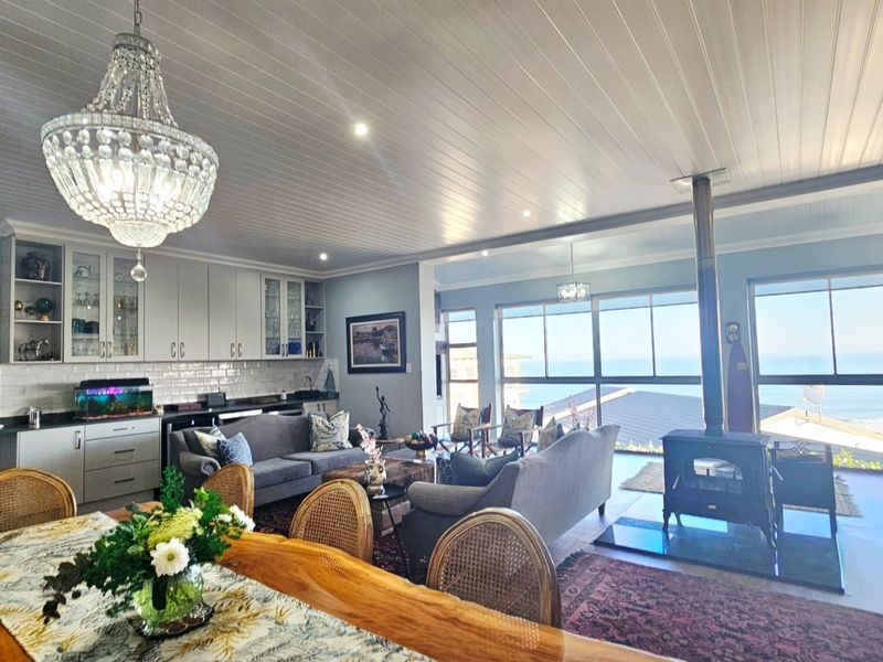 Spacious open-plan living and kitchen area featuring a wood-burning fireplace, modern cabinetry, and expansive windows with ocean views.