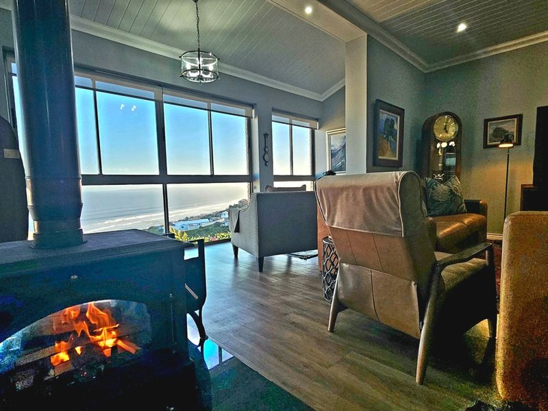 Spacious living room featuring a cozy wood-burning fireplace, large windows with panoramic ocean views, and modern timber-look flooring.