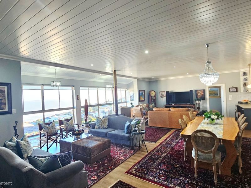 Spacious open-plan living and dining area featuring a wood-burning fireplace, tongue and groove ceilings, and large windows with expansive coastal views.