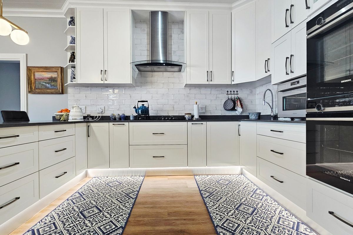 Modern, well-appointed kitchen featuring white shaker-style cabinetry, subway tile backsplash, integrated appliances, and sleek stone countertops with under-cabinet lighting.