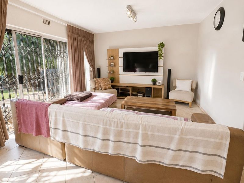 A bright living room featuring tiled flooring and a sliding glass door with security gate, providing direct access to the outdoor area.
