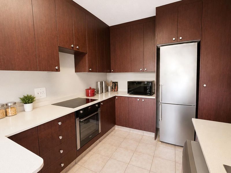 A well-maintained kitchen featuring dark wood cabinetry, stone countertops, integrated electric hob, built-in oven, and stainless steel refrigerator with tiled flooring.