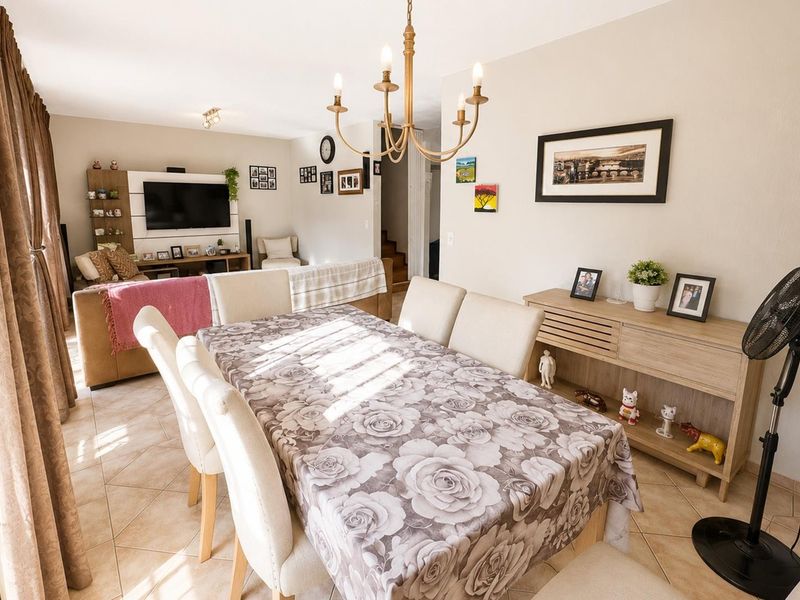 Open-plan living and dining area featuring tiled flooring, a central chandelier, and a built-in media unit, creating a functional and connected living space.