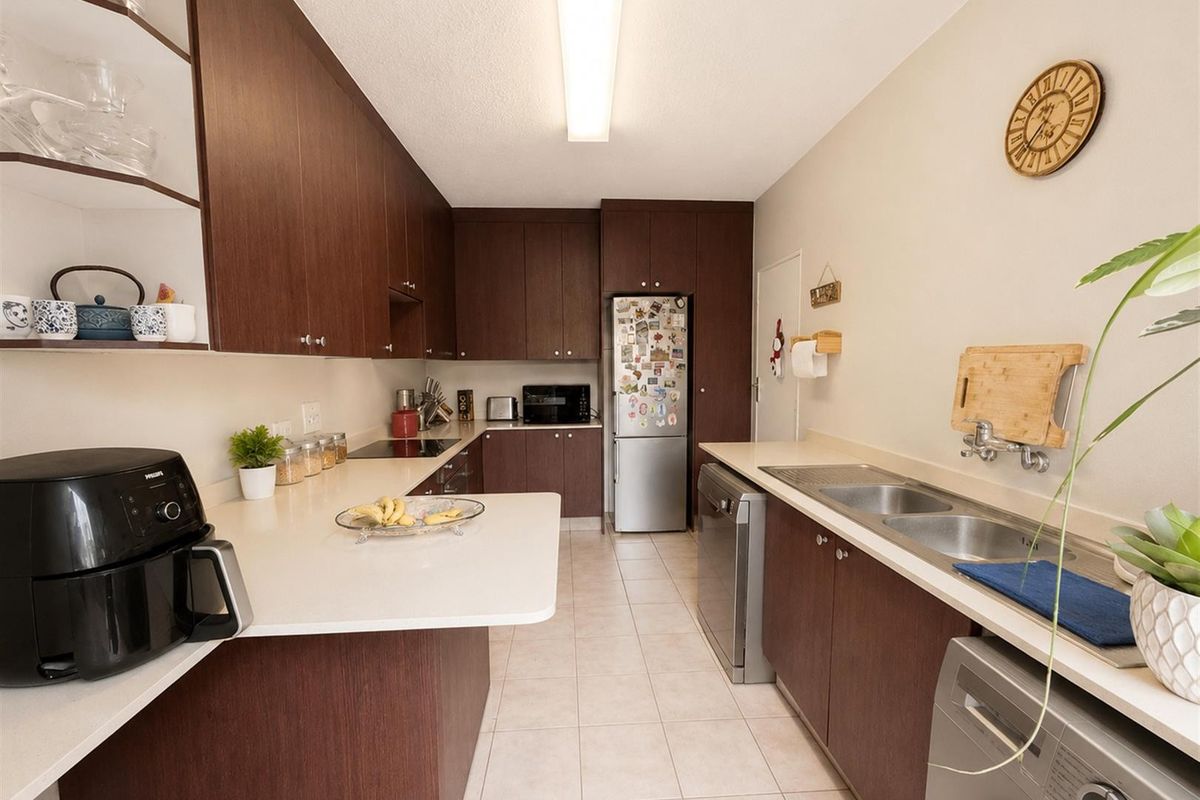 A functional kitchen featuring dark wood-look cabinetry, light solid surface countertops, a double basin sink, and integrated appliances with ceramic tiled flooring.