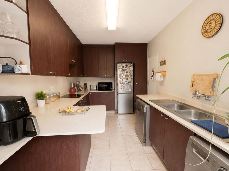 A functional kitchen featuring dark wood-look cabinetry, light solid surface countertops, a double basin sink, and integrated appliances with ceramic tiled flooring.